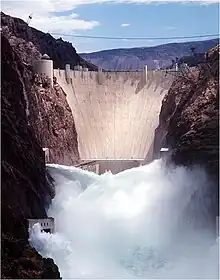 Front view of a dam in a narrow canyon, with water shooting out of the gates