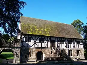 Two story building with half timber second floor built over the stone first floor. Wooden staircase goes to the entrance on the second floor.