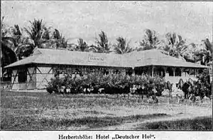 small single story building, grass roof, veranda, bushes