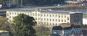 A very long white building sits on a small body of water, partially obscured by trees.