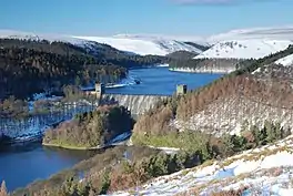 Image of a dam head with a lake beyond, surrounded by snow-capped hills