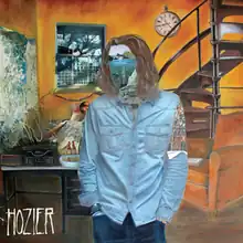 A painting of a auburn-haired man who wears a light blue shirt and blue jeans is standing beside a room. His face and left shoulder are covered by two different paintings and the word "Hozier", stylized in all capital letters, is placed on the lower left corner of the picture.