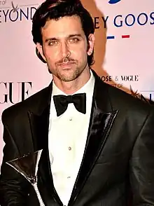 Roshan with a trophy in his hand in a tuxedo as he directly looks at the camera.