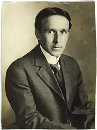 A seated man, wearing a suit and tie