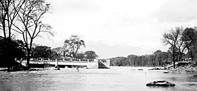 A destroyed bridge with a part with one end attached to the shore and the other end in the water; the other part is missing.