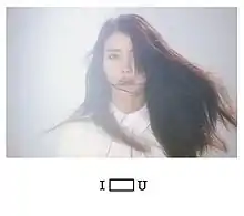 In the centre of a white page is a blue-lit rectangle with a mid-shot of a woman with long dark hair partially covering her face. Underneath the picture in the middle is the title I U, with an elongated box in the middle.