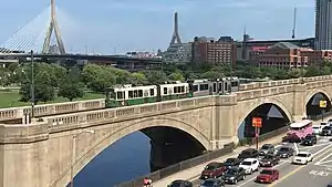 A light rail train on a concrete arch viaduct in an urban area