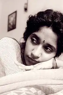 close-up, sepia image of Indira Tiwari resting her head on her arms, looking sideways to the right