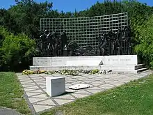 Simple sculpture of dark human figures against a fence