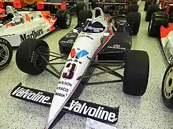 A black and white racing car adorned with sponsors logos and the number 3 in black on the front wing sitting in a museum