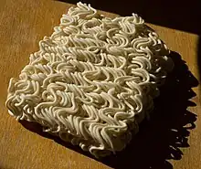 A brick of uncooked instant ramen noodles on a wooden table