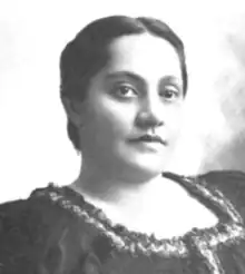 A young Hawaiian woman, dark hair parted center and dressed to the nape, wearing a dark dress with a square ruffled collar