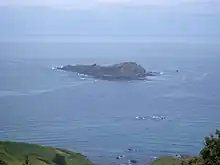 A small rocky island. A sail yacht can be seen behind it for size comparison.