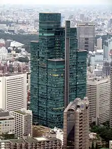 Aerial view of a green, glass high-rise composed of square sections that rise to differing heights