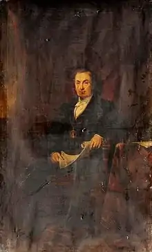 Seated man wearing dark suit and holding some papers