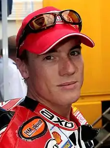 A man in his mid-20s wearing an red baseball cap and motorcycle overalls