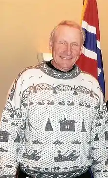 Man in light gray winter style sweater standing in front of Norwegian flag