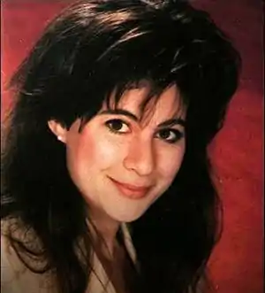 A woman with long dark hair and brown eyes against a red background