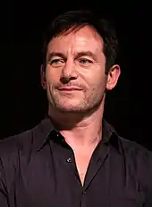 A man with short black hair and a black shirt, and he is smiling.