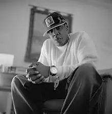 A black-and-white picture of an African-American man wearing a white shirt, trousers, a cap, and a wristwatch