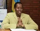 Jeannette Kagame shown sitting at a desk at a public event, wearing a green jacket