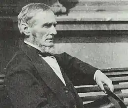 man sitting on bench in profile looking right holding top hat