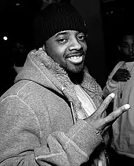 The black-and-white portrait of an African-American man smiling. He is wearing a gray coat and a black cap.