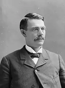 Head of a 40sh man with gray hair, squinting through eyeglasses