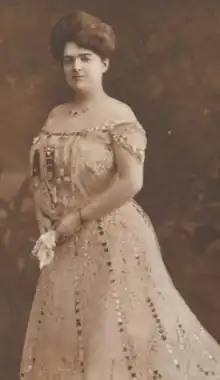 A white woman with dark hair, in a bouffant updo, wearing an off-the-shoulder gown embellished with sequins.