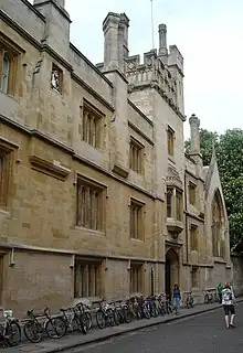 A three-storey building, topped by a tower, and many bicycles leaning against the wall