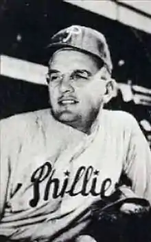 A black-and-white photograph of a man with glasses wearing a dark baseball cap and pinstriped baseball uniform with "Phillies" in script across the chest