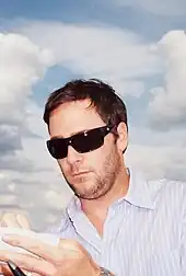 A man in his early thirties signing his autograph for a fan. He is wearing sunglasses and a striped shirt