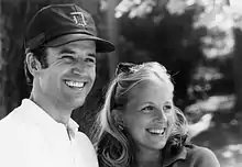 Black and white outdoor photo of Joe and Jill Biden in everyday clothing, both smiling and looking past the camera to the right