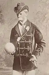 elderly-looking white man with large white moustache holding a ball and looking sternly at some unseen person or thing