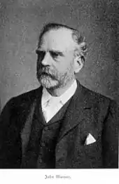  Head and upper body of elderly bearded man, facing left, wearing a dark suit with exposed white handkerchief in the breast pocket