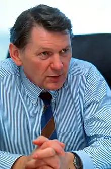 John Barnard wearing a light blue striped shirt and a navy blue and beige tie