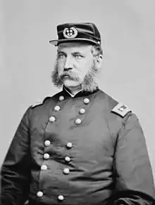 Black and white photo of a man with a moustache and mutton-chop sideburns. He wears a dark military uniform and a kepi with the two stars of a major general.