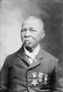 Head and shoulders of an older black man with short hair and a mustache, wearing a suit coat with three medals hanging from ribbons on the left breast.