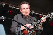 John Paul Jones playing the mandolin atop a stage.