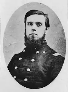 Black and white photograph shows a dark-haired young man with a beard, but no moustache. He wears a dark uniform with two rows of buttons.