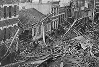 Black and white photo of a row of buildings with broken wood in front