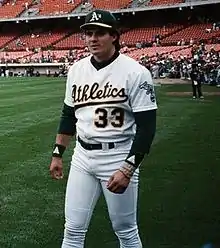 A man in a white baseball uniform and green undersleeves and cap