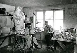 A photograph of Josef Ekberg (left) and Gunnar Wennerberg (right), seated and painting vases in the Gustavsberg Porcelain Factory, around 1900.