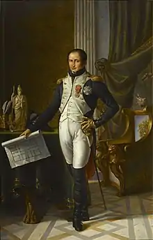 Painting shows a slightly balding man with dark hair standing in a room holding a building plan. He wears an early 1800s French military uniform: a blue coat with a white waist coat, white breeches, and black boots which rise above his knees.