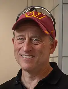 Man smiling while wearing a baseball cap featuring a Washington Commanders logo with sunglasses resting on top.