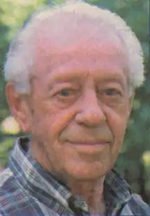 Photo of an elderly man, balding with white hair, and wearing a plaid shirt