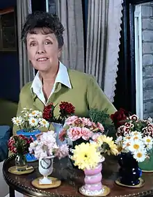 slim white woman of mature years seated by a table that is covered with flowers