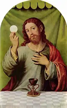  Oil painting showing Jesus at the Last Supper. He is shown seated behind a table, looking directly at the viewer while raising a communion wafer in his right hand, and laying his left hand on his heart. The cup of Communion is on the table, placed centrally in the picture.