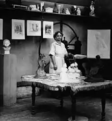 A woman standing in an art studio, wearing a light-colored dress