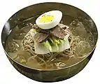 Naengmyeon (cold noodles) topped with boiled egg, pyeonyuk, cucumber, and pickled radish